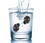 Waterproof wireless earbuds submerged in a glass of water demonstrating water resistance.