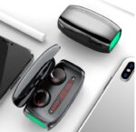 True wireless earbuds in an open charging case with LED display, shown in a modern setup with smartphones.